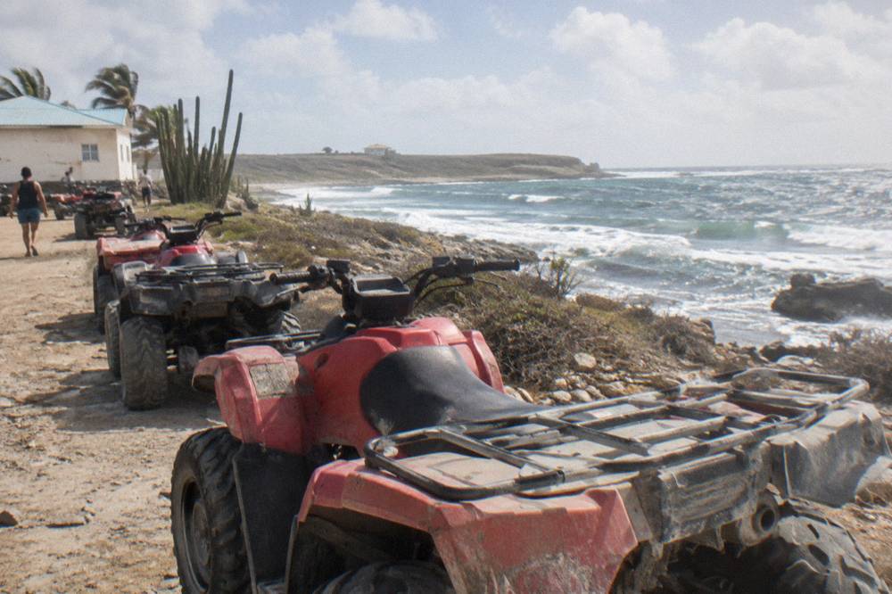 A row of parked four-wheel all-terrain vehicles lined up on a dirt lot near a coastal road