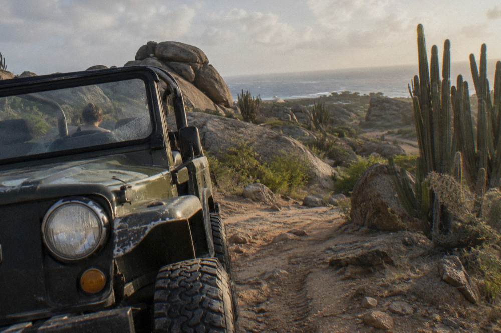 An open-air four-wheel-drive jeep crossing a rocky desert track lined with cacti