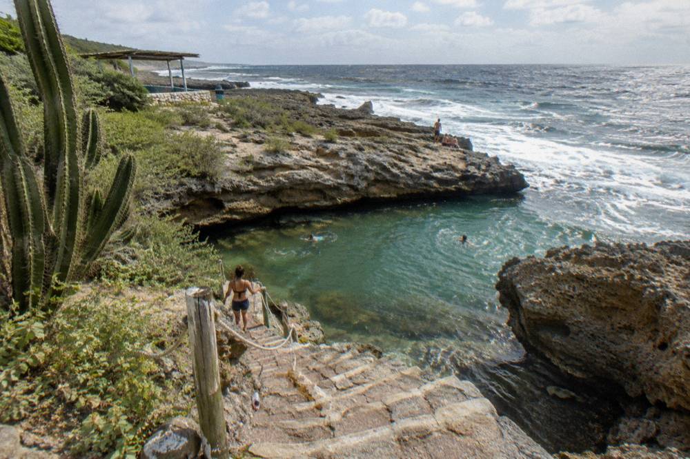 Clear green water in a volcanic rock pool with rocky steps leading down toward the water