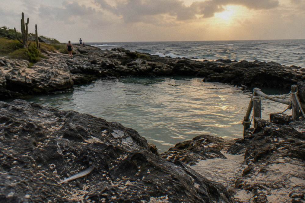 A calm natural pool enclosed by dark rock with the open ocean horizon beyond the rim