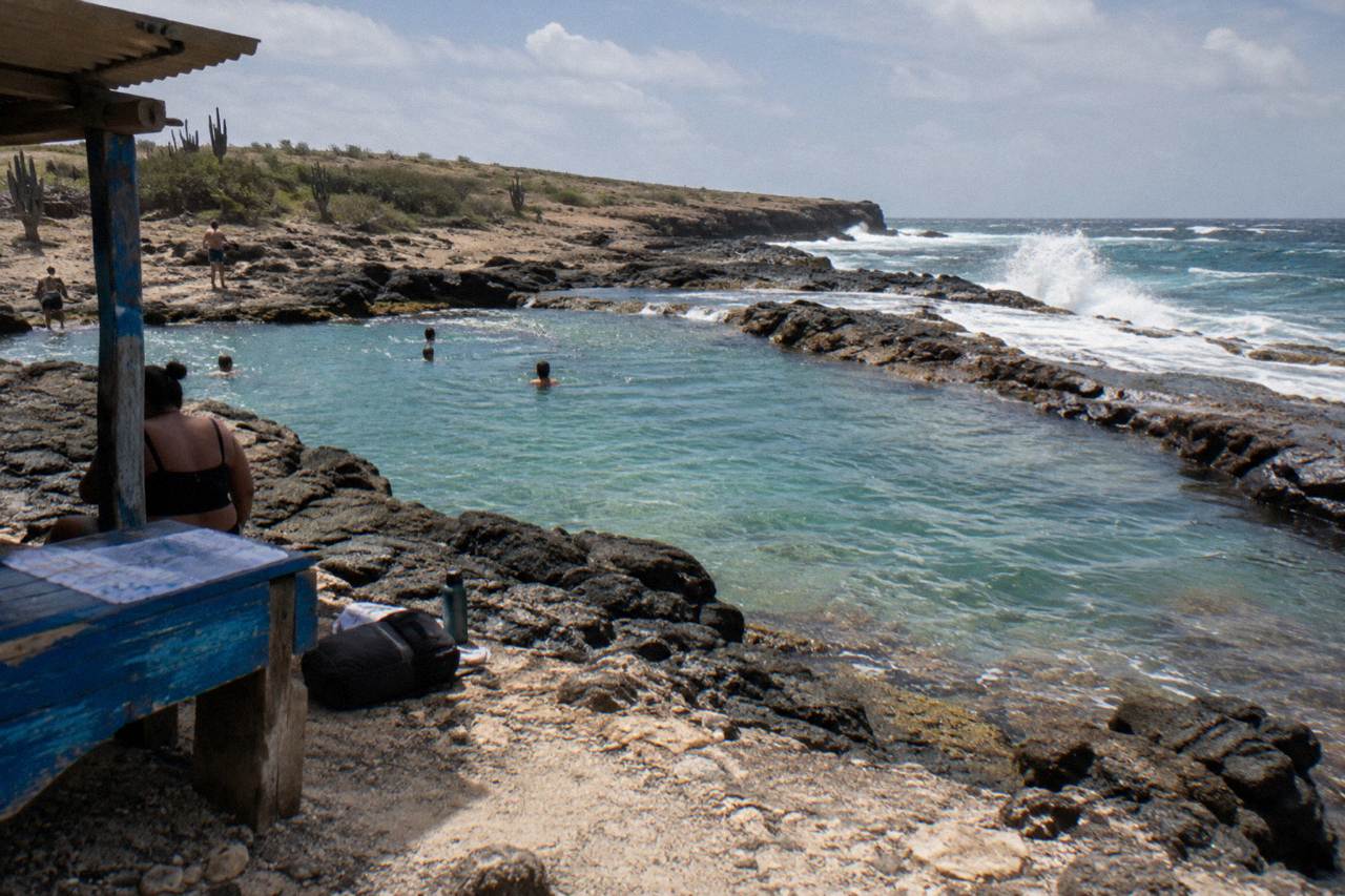 A natural rock pool on a volcanic shoreline with calm turquoise water and waves breaking on the outer rocks