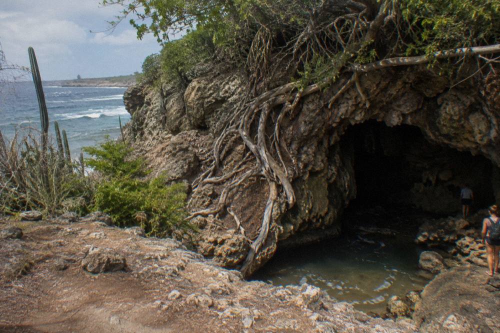 Dark limestone cave opening framed by weathered rock on a dry hillside