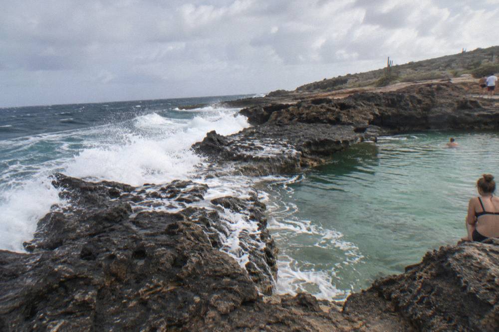 Dark volcanic shoreline with waves breaking against rocks near a calm rock pool