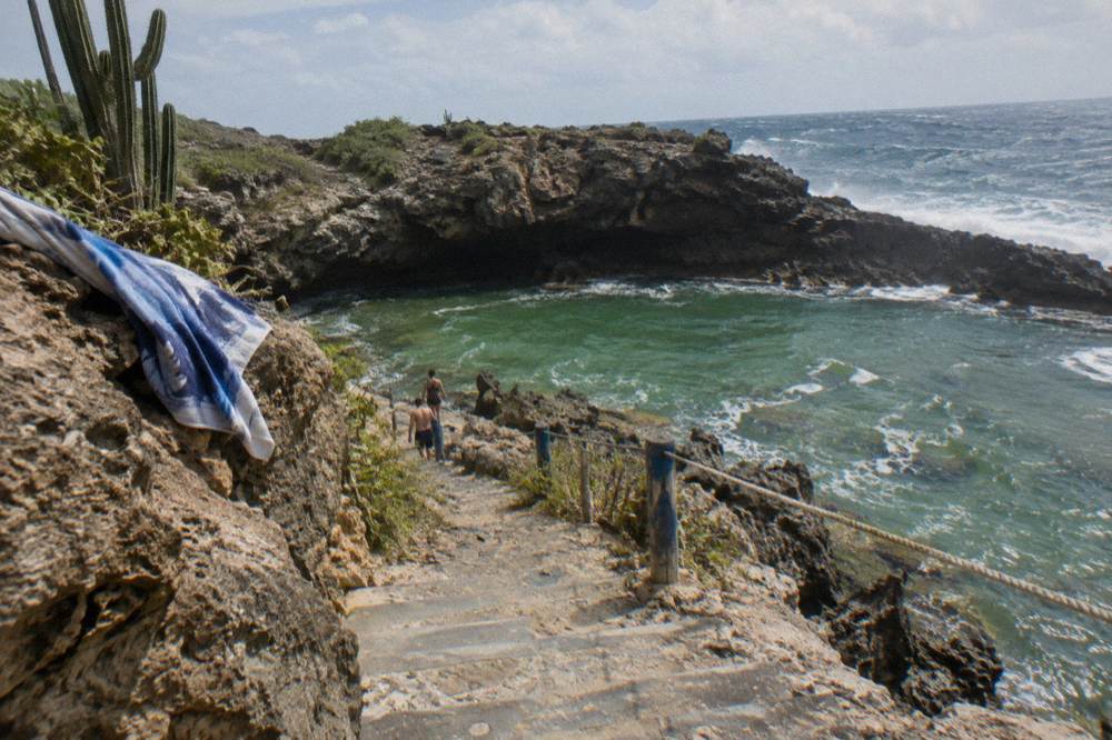 Hikers descending stone steps toward a rock-ringed natural pool at morning light