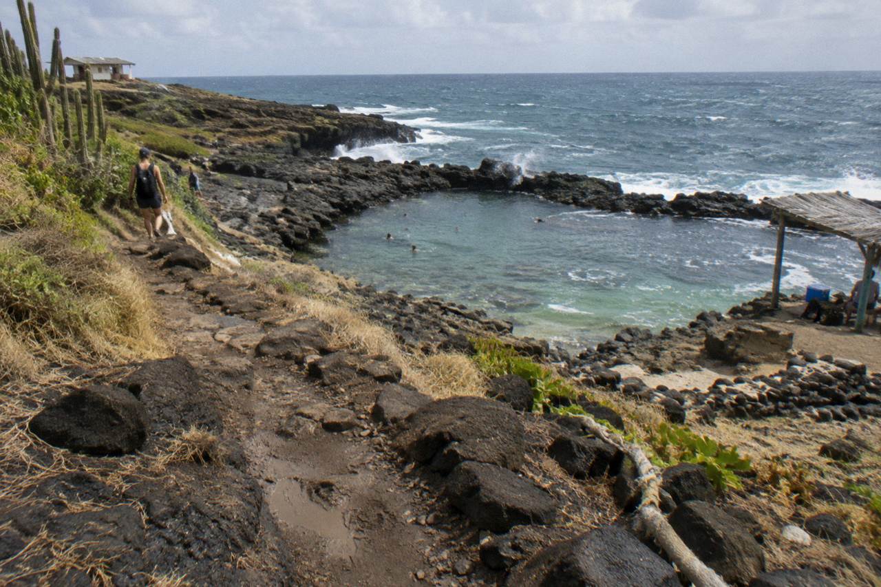 Rough volcanic trail winding along Aruba's north-east coast toward a rock-ringed pool
