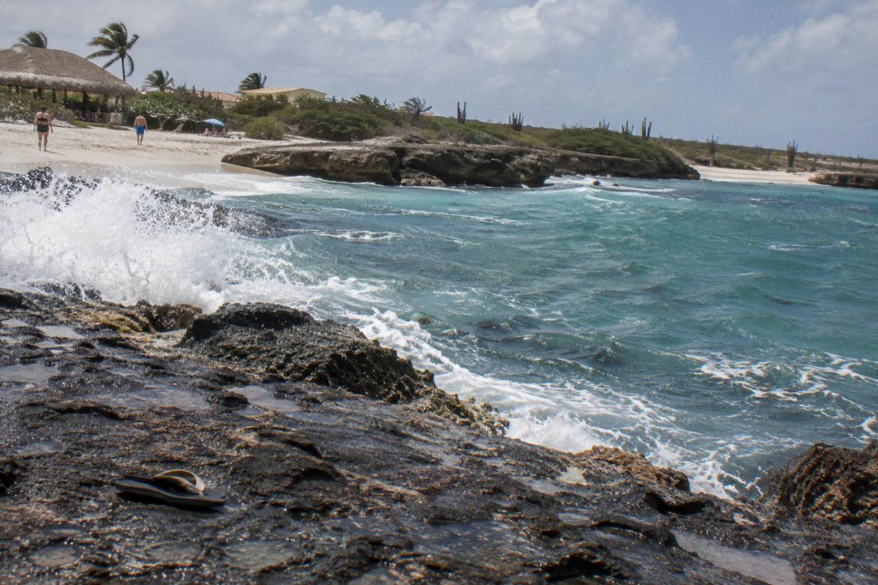 Rocky volcanic coastline in Aruba with waves splashing over dark stone