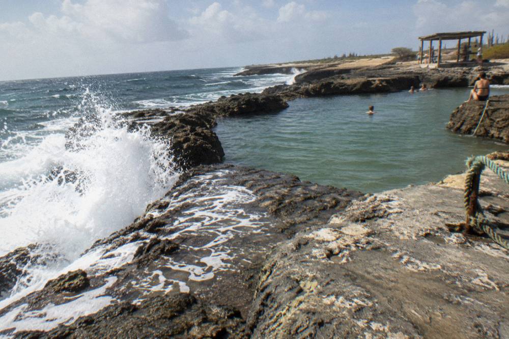 Rocky volcanic shoreline with waves breaking against dark stone and a calm pool beyond