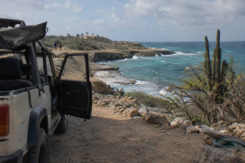 Parked open-air four-wheel-drive vehicle on a gravel pullout above a rocky cove