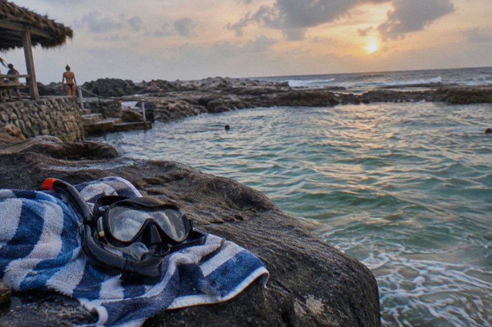 Snorkel mask and towel resting on smooth dark rock beside still turquoise water
