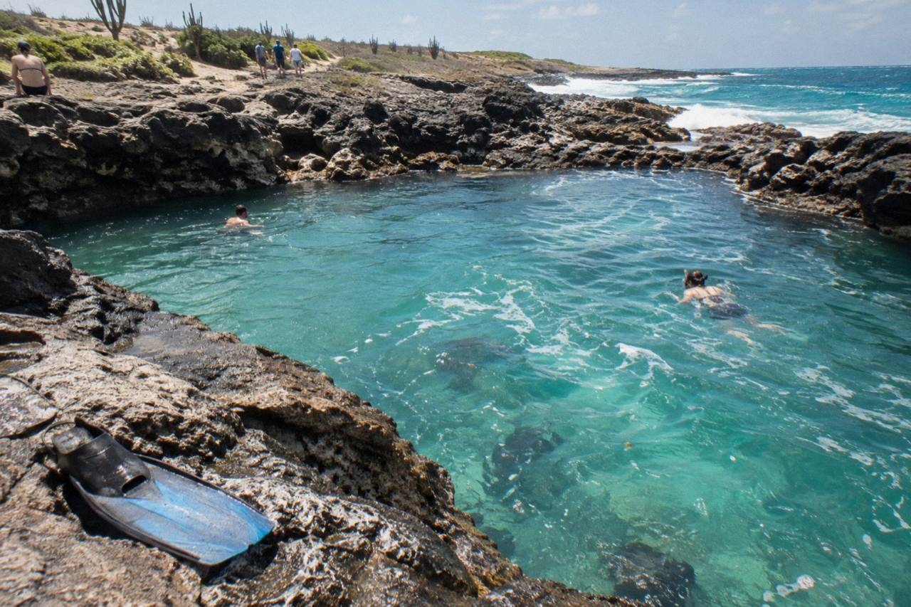Turquoise water filling a natural rock basin on a rocky coastline under a clear sky