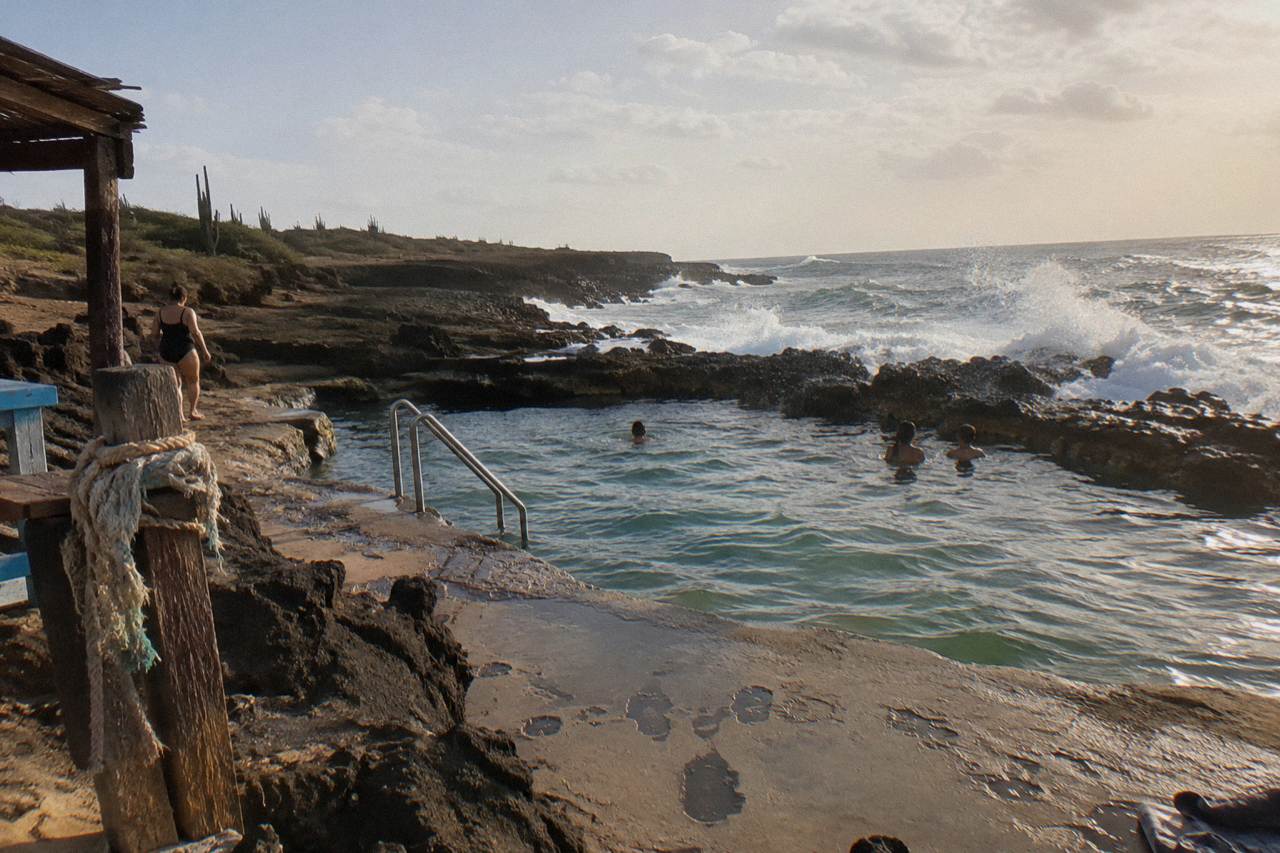 A natural rock pool on a volcanic coastline with waves breaking against the dark stone rim under an open sky