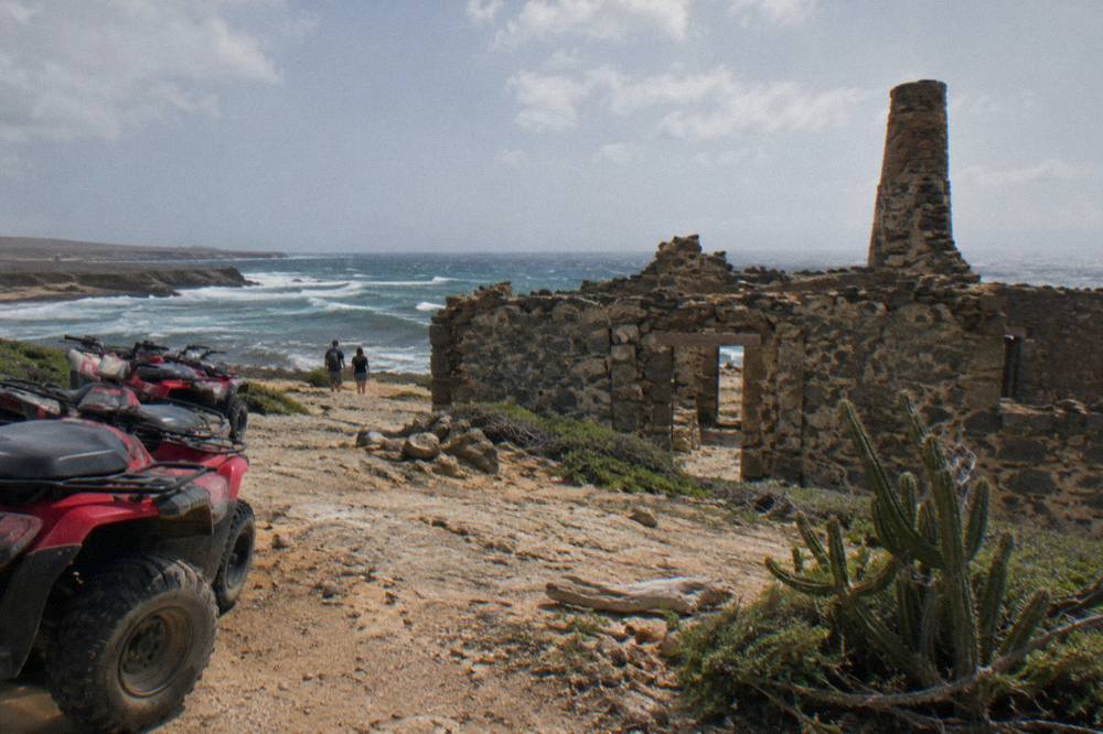 A guided line of quad vehicles parked on a dirt track beside weathered coastal rock