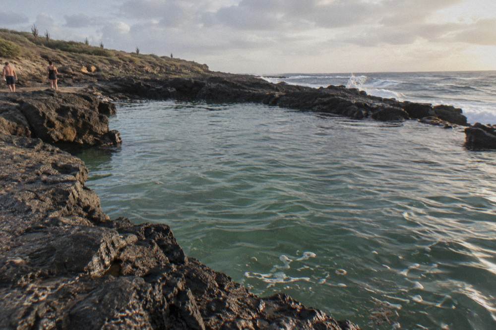 A quiet natural rock pool ringed by dark volcanic stone along the coast