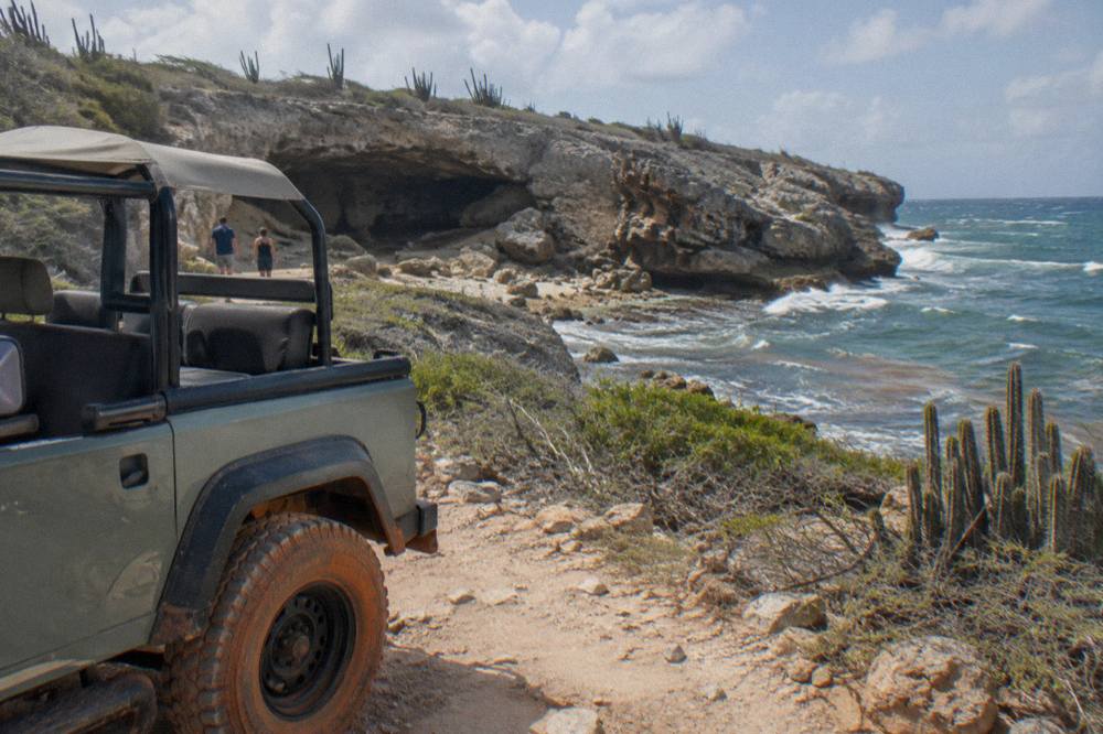 An open-air four-wheel-drive jeep parked on a rough dirt track beside desert scrub and volcanic rock
