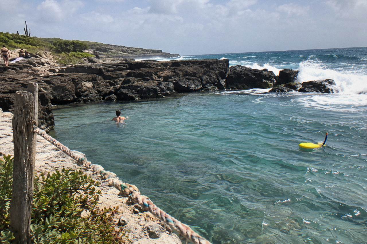 Rocky volcanic shoreline with a calm natural pool set among dark stone on Aruba's north-east coast