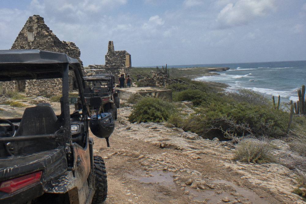 A line of UTVs parked on a dusty coastal trail with flat rock and scrubland stretching to the shoreline