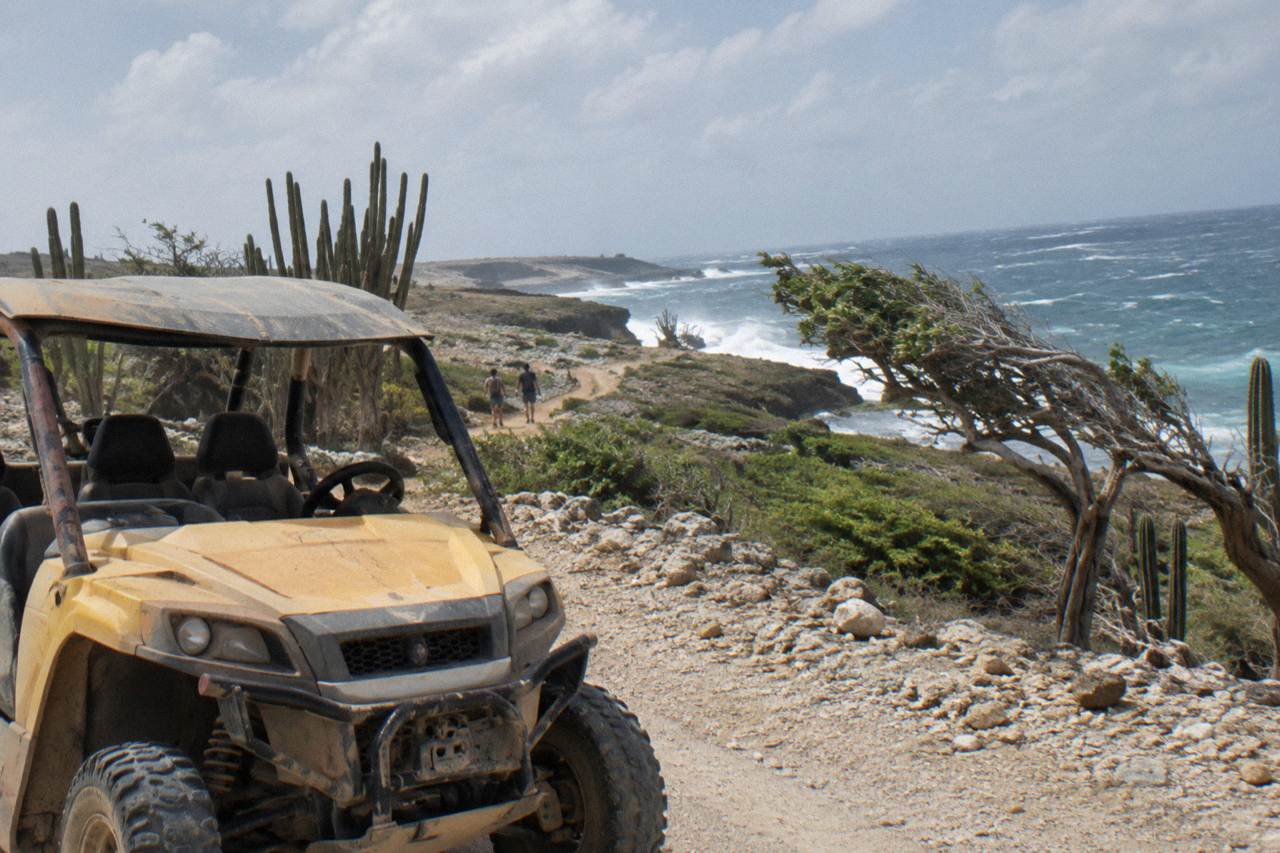 A UTV parked on a rocky dirt track along Aruba's north coast with open sky and cactus scrub