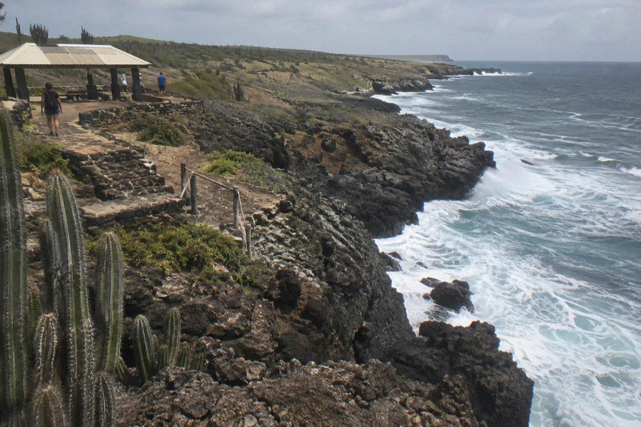 Rocky volcanic coastline of Arikok National Park with waves breaking against dark stone cliffs under an open sky