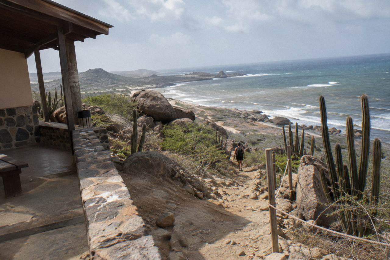 A dry hiking trail winding through rocky desert terrain toward the Aruba coastline