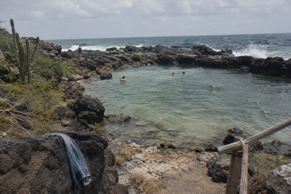 A clear shallow pool ringed by dark rock with ocean waves beyond