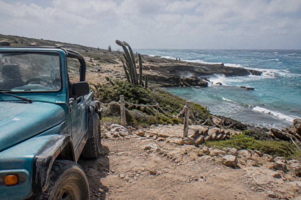An open-air jeep parked on a rocky coastal plateau near a stone staircase