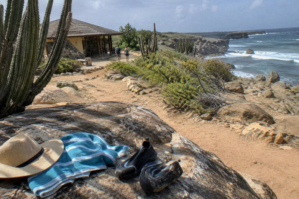 Water shoes, a towel and a sun hat arranged on a rock beside a dusty trail in Arikok National Park