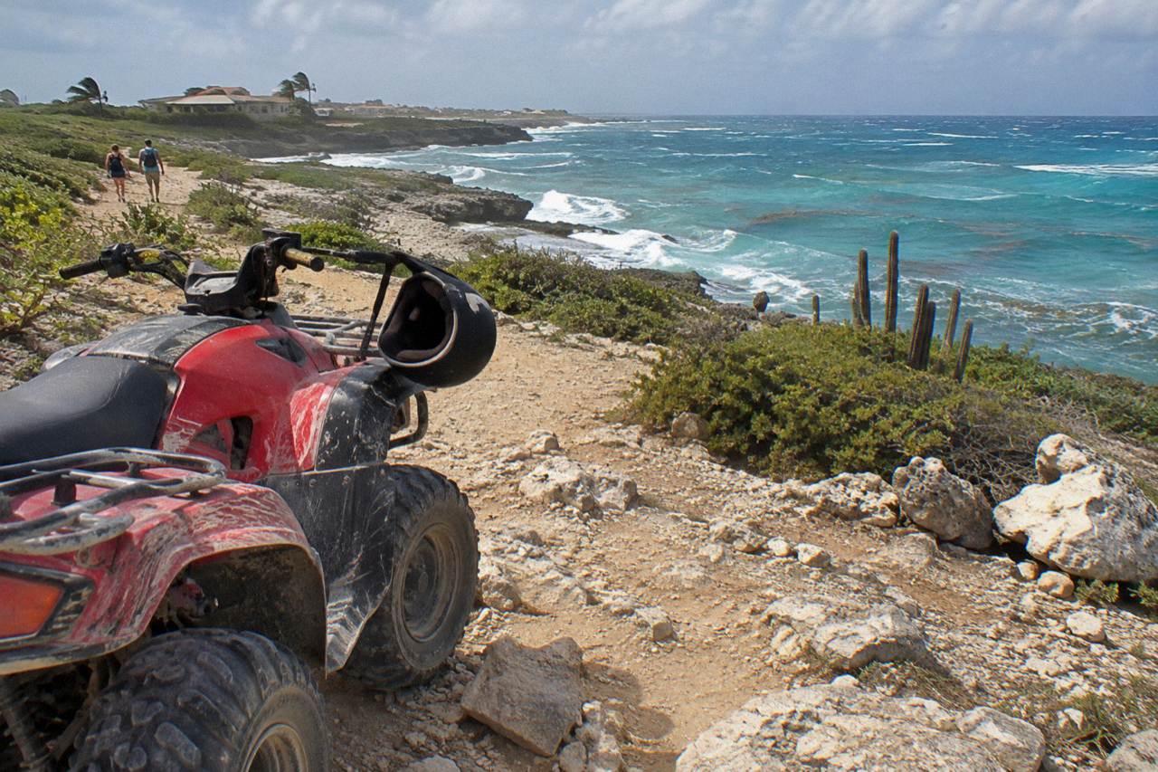 An all-terrain vehicle parked on a rocky desert trail above a turquoise Caribbean coastline