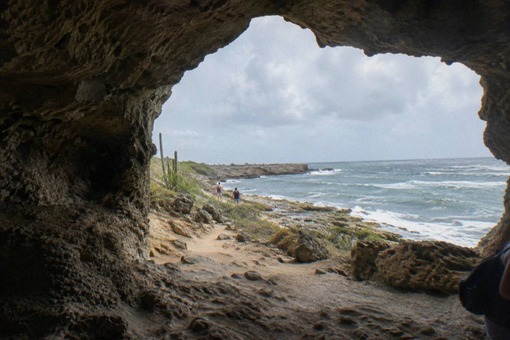 Wide cave entrance with rough limestone walls and daylight filtering in