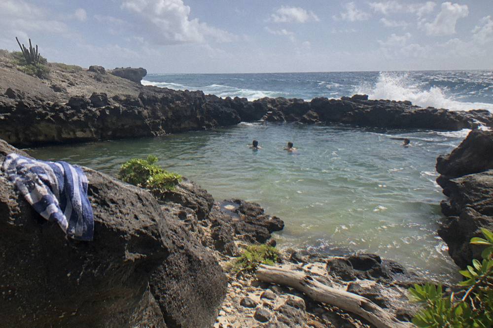 Shallow rocky pool surrounded by dark volcanic stone with waves beyond