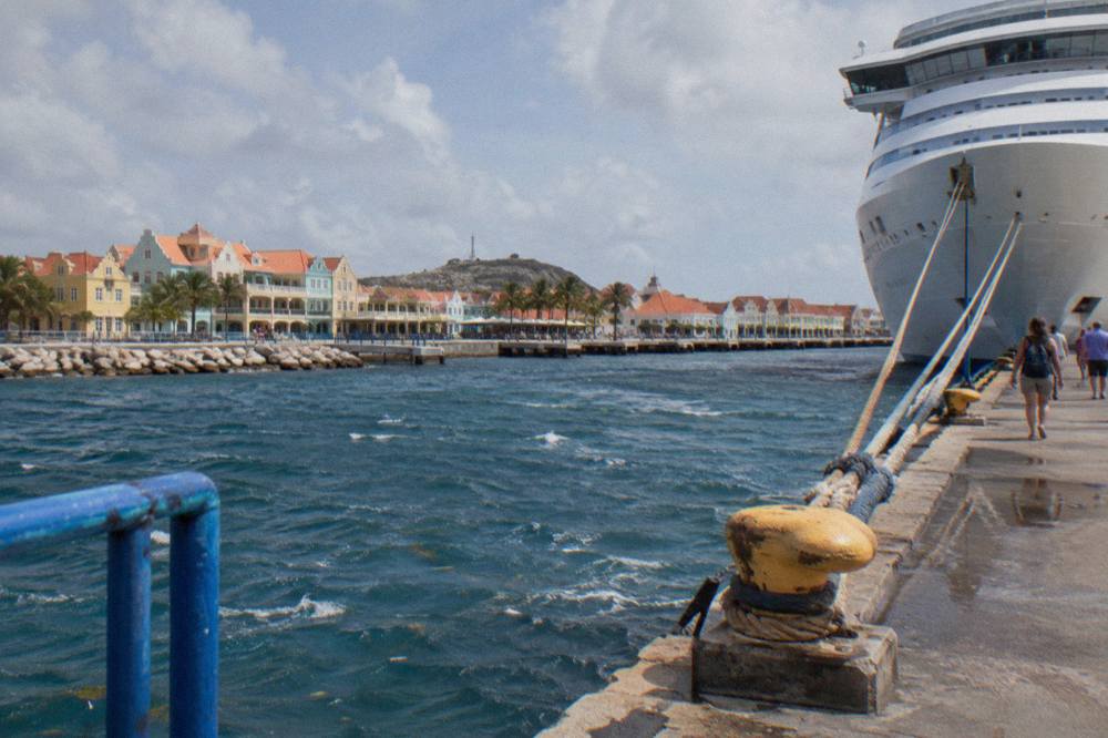White cruise ship docked at a pier beside pastel-colored waterfront buildings in Oranjestad