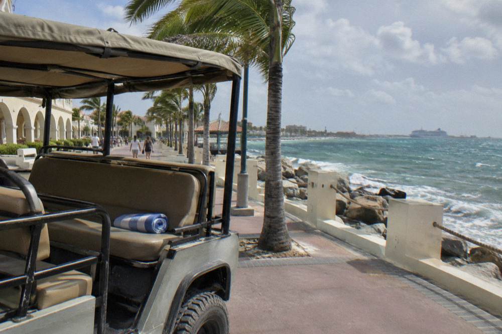 Open-air safari jeep with canopy parked beside a cruise terminal promenade in Oranjestad