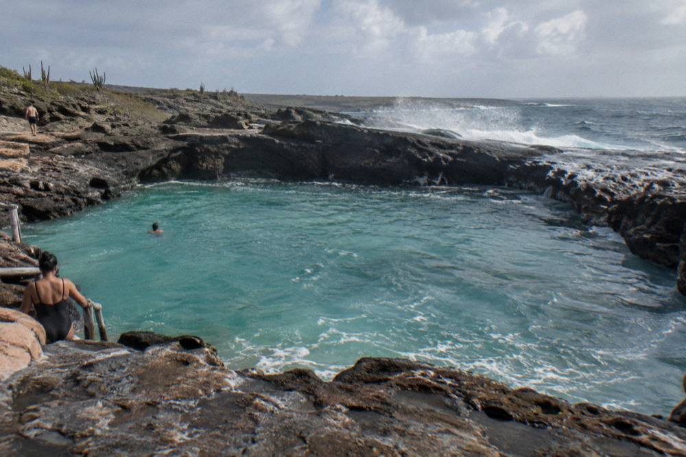 Calm turquoise water filling a volcanic rock basin with gentle spray over the dark stone rim
