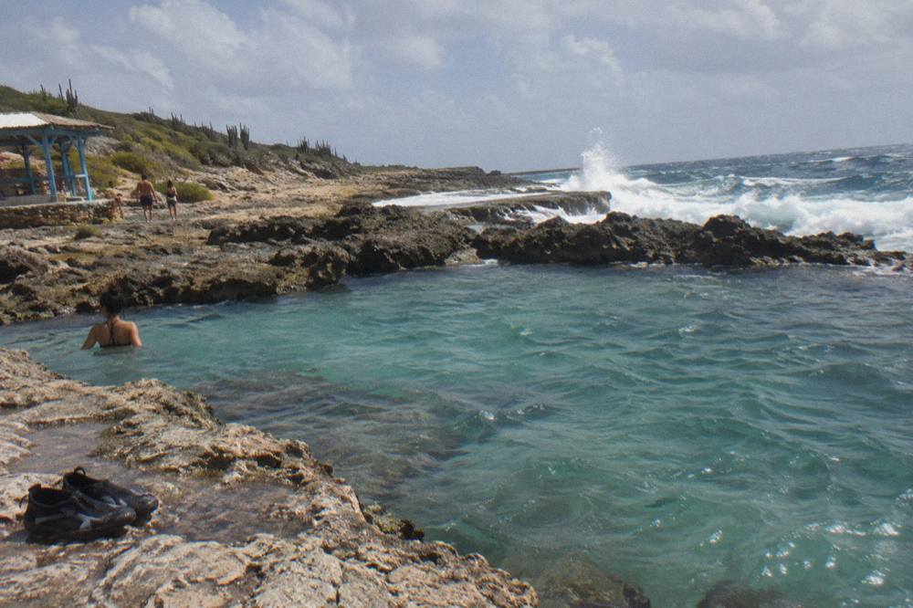 Turquoise water filling a volcanic rock pool with waves breaking on the rocky coast behind it