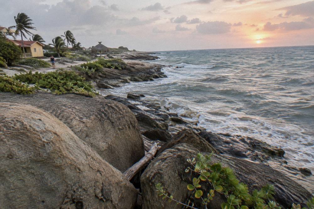 Rocky Tropical Coastline At Sunrise With Waves Breaking Against Boulders And Palm Trees