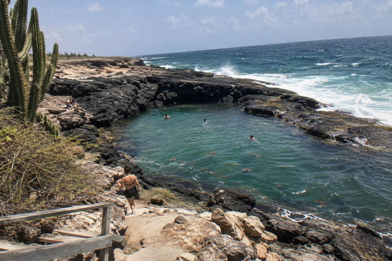 Rocky volcanic shoreline with a natural pool basin set below coastal cliffs under a clear sky