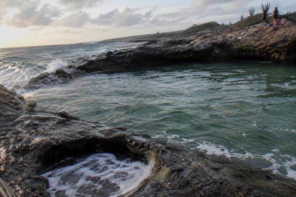 A quiet volcanic rock pool enclosed by dark stone with gentle waves breaking beyond the rim