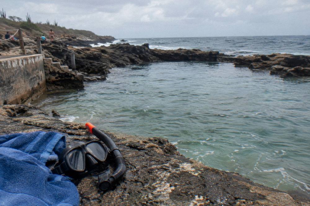 Snorkel mask and towel resting on volcanic rocks beside a calm natural basin