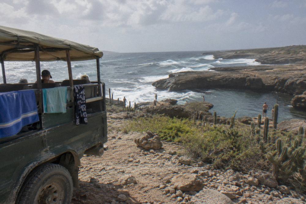 An open sided safari jeep parked on a rocky plateau above a natural rock pool on a rugged coastline
