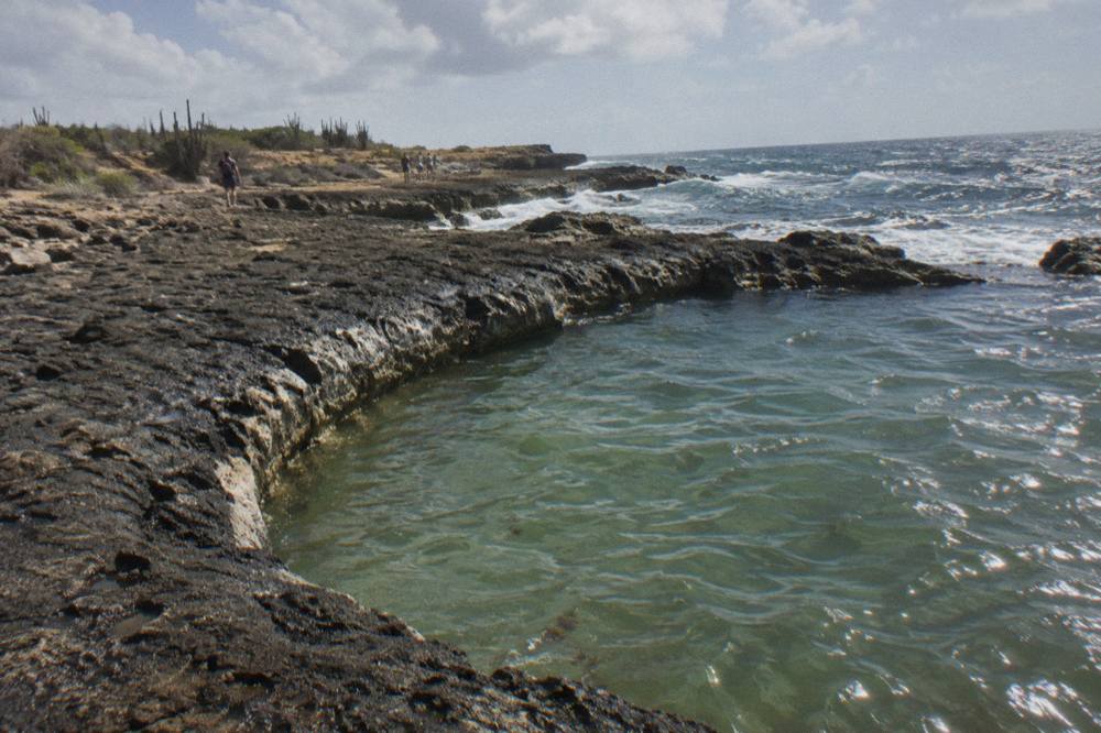 Dark volcanic rock forming a curved rim around a calm natural pool with the open sea beyond
