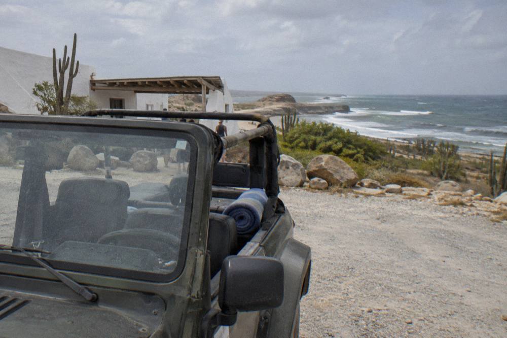 Open-air four wheel drive vehicle parked on a rocky desert track near the coast