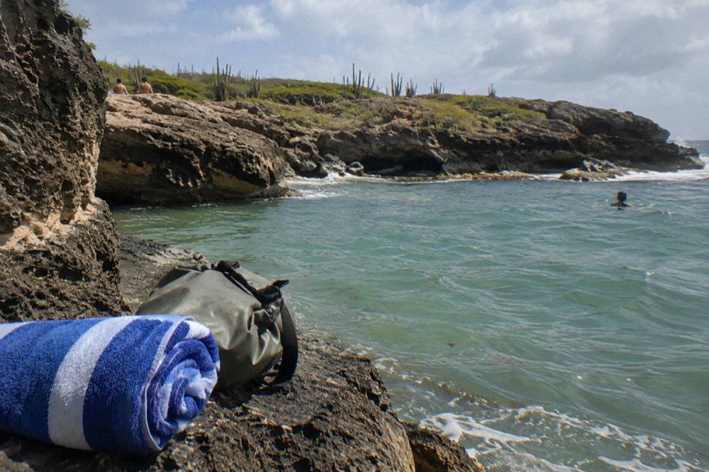 Beach towel and dry bag on a rock ledge above a calm natural basin