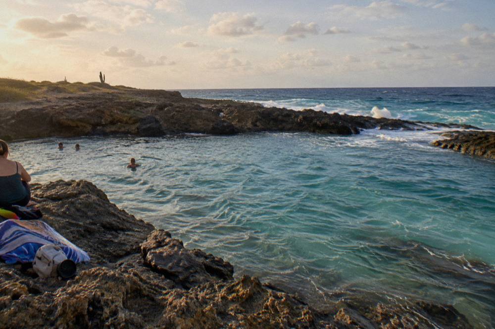 Turquoise water filling a volcanic rock basin on the north-east coast, waves breaking on the outer reef beyond