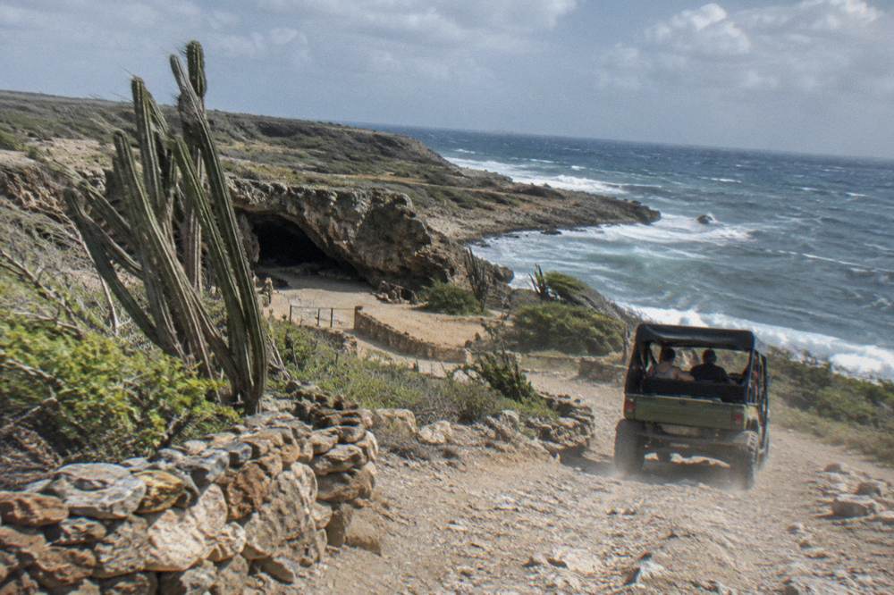 An open-air four by four vehicle on a rocky track descending toward a volcanic coastline inside a national park