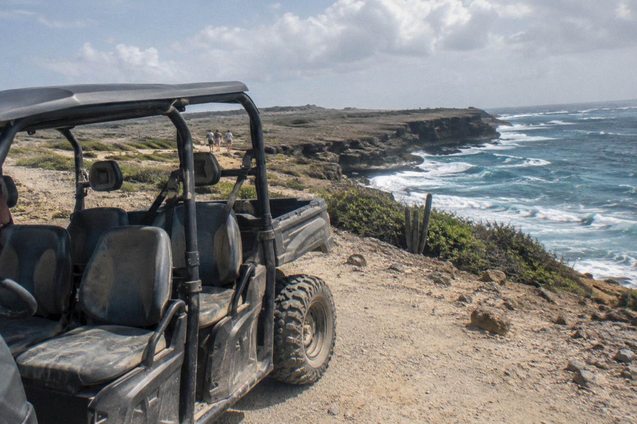 A four-seat utility terrain vehicle parked on a rocky dirt track above Aruba's windswept north coast shoreline