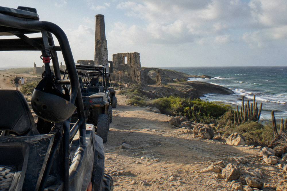 A line of side-by-side UTV buggies parked on a dirt trail beside weathered limestone rock formations on Aruba's north coast