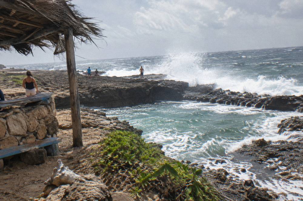 Waves breaking over a dark volcanic rock rim into a sheltered coastal pool