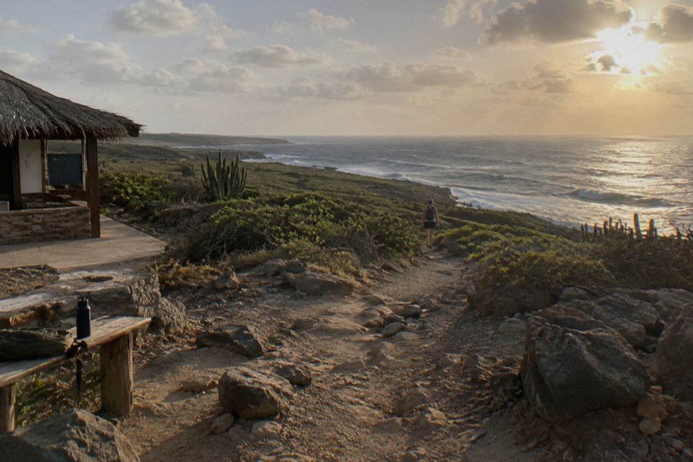 A hiking trail across dry rocky terrain toward a sunrise over the sea