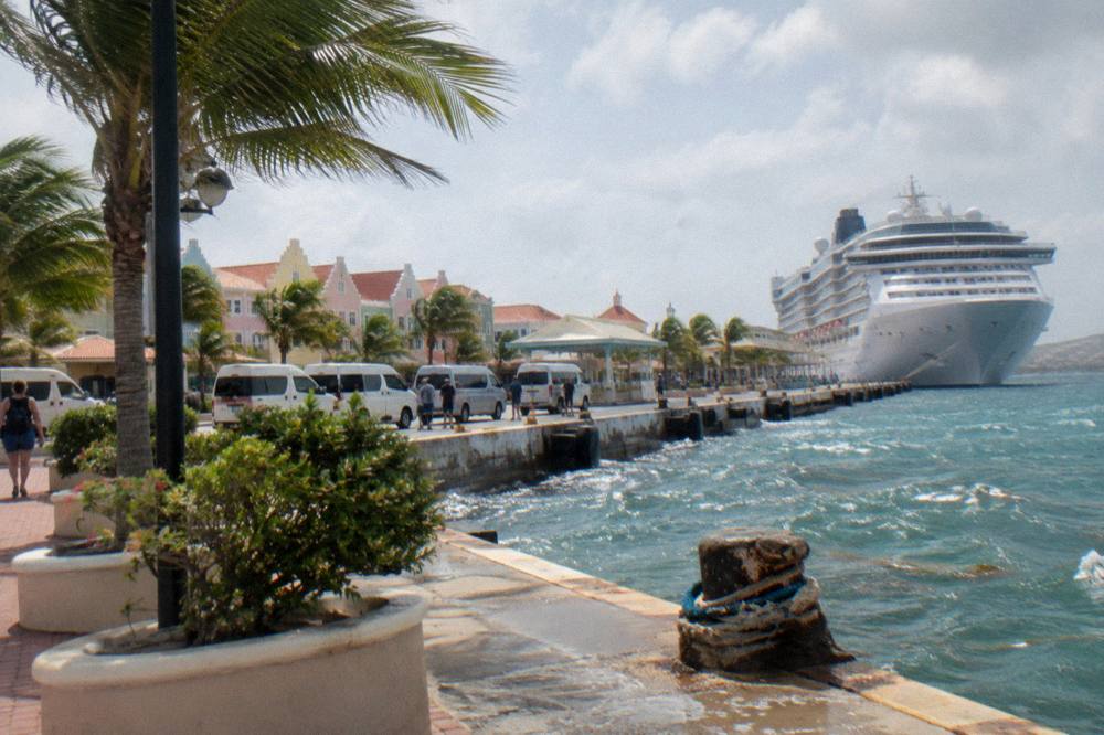 A cruise ship docked along a waterfront street with tour vans waiting nearby