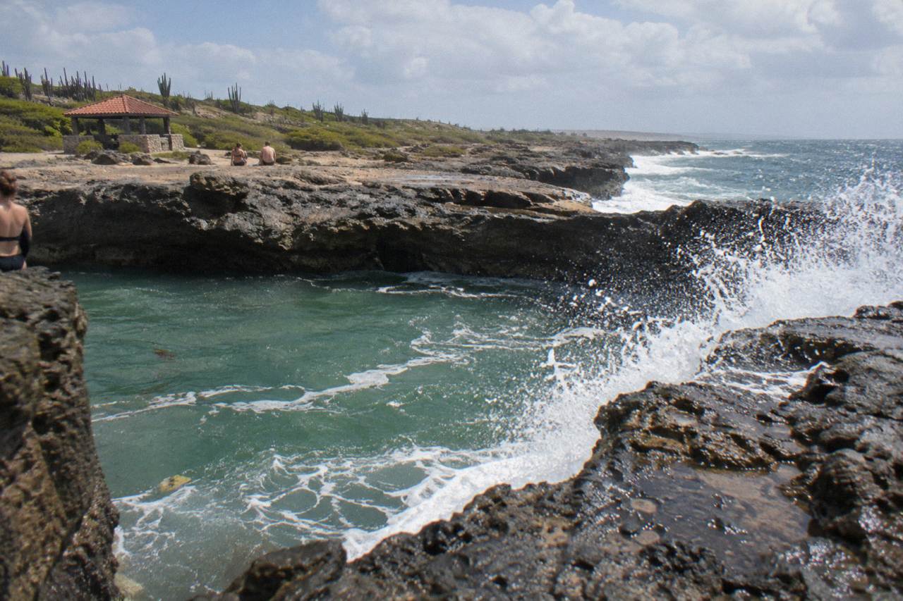 A natural rock pool on a volcanic coastline with waves spraying over the rim under morning light
