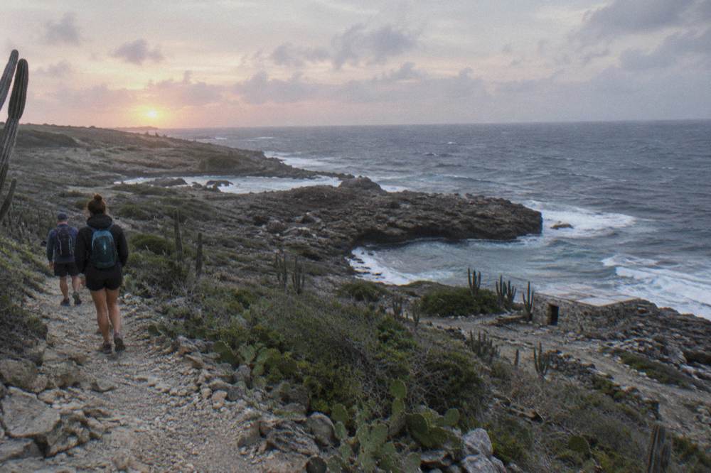 Hikers walking a stony path at first light above the Caribbean coastline